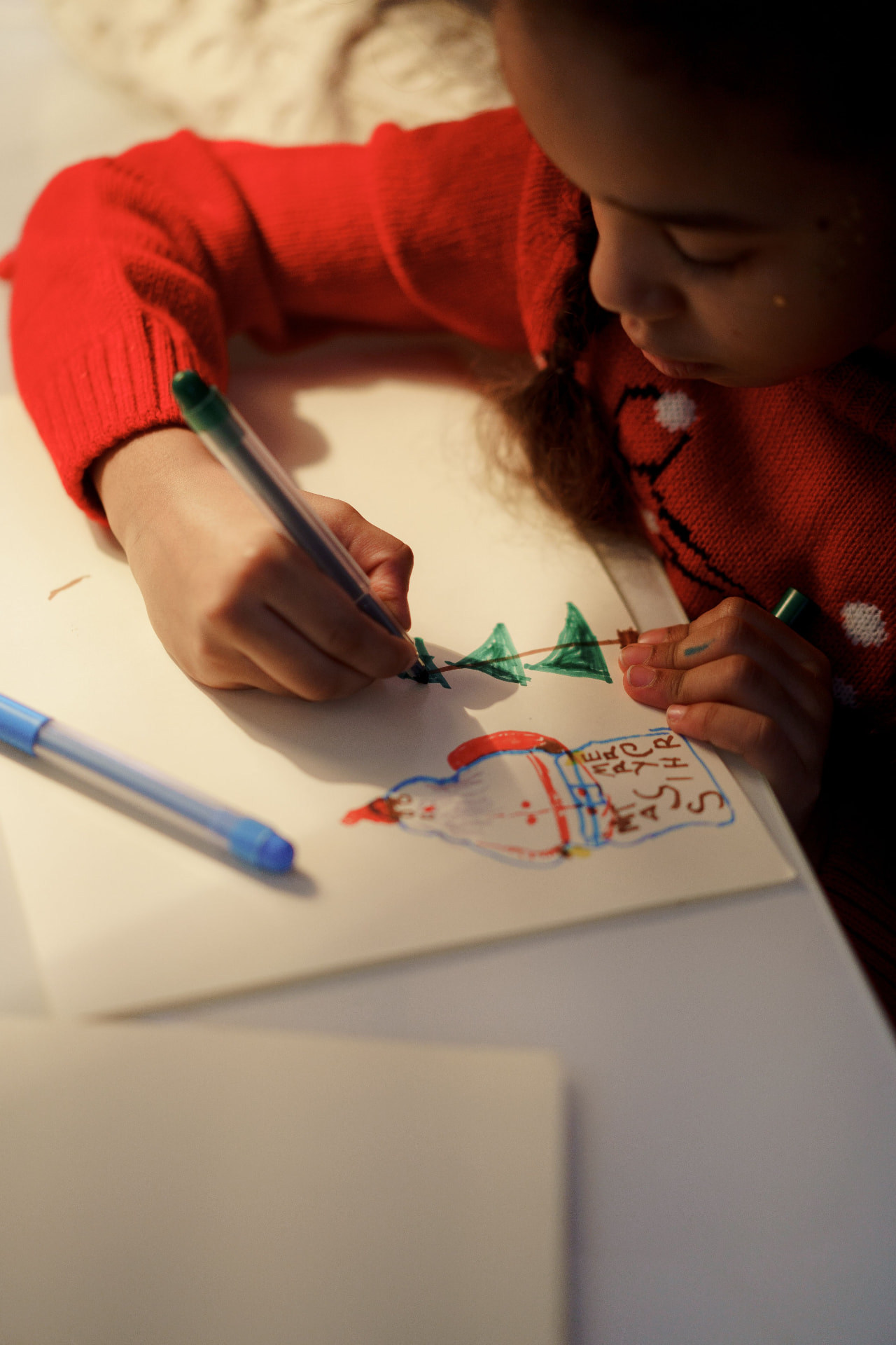 A child in a red sweater drawing Christmas trees on paper