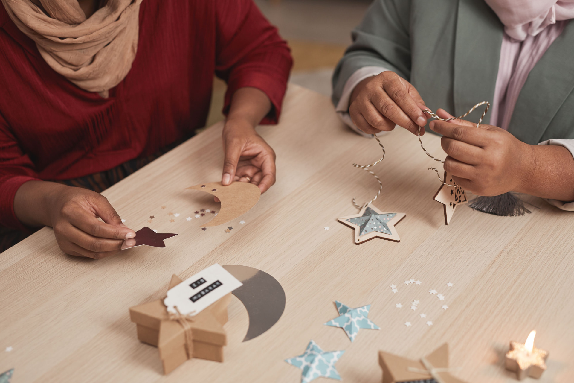 Hands crafting wooden star and moon ornaments at a holiday craft table