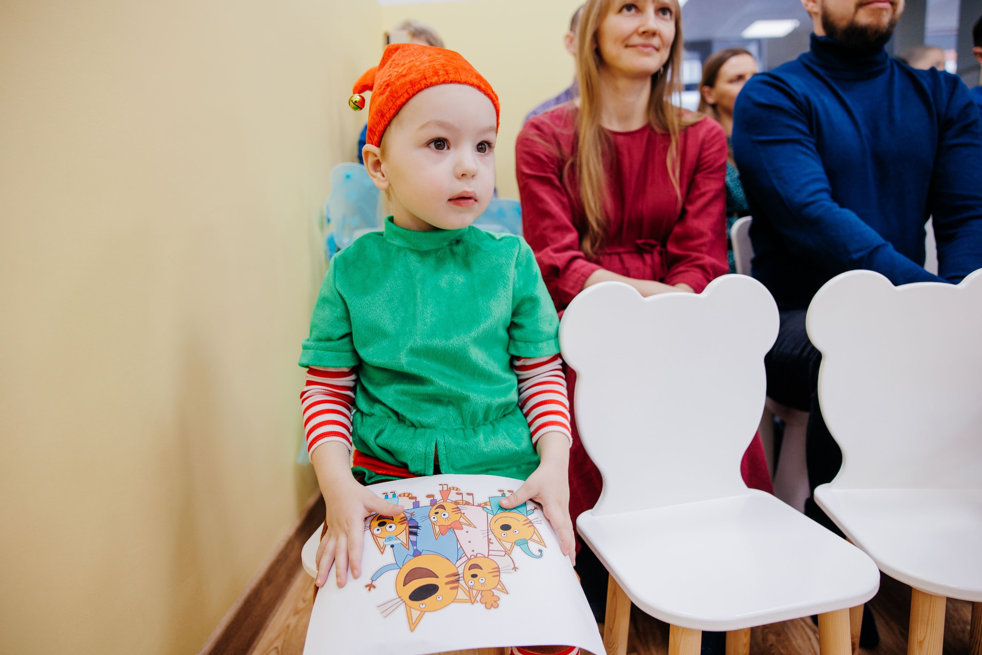 A young child in an elf costume holding a picture at a holiday event